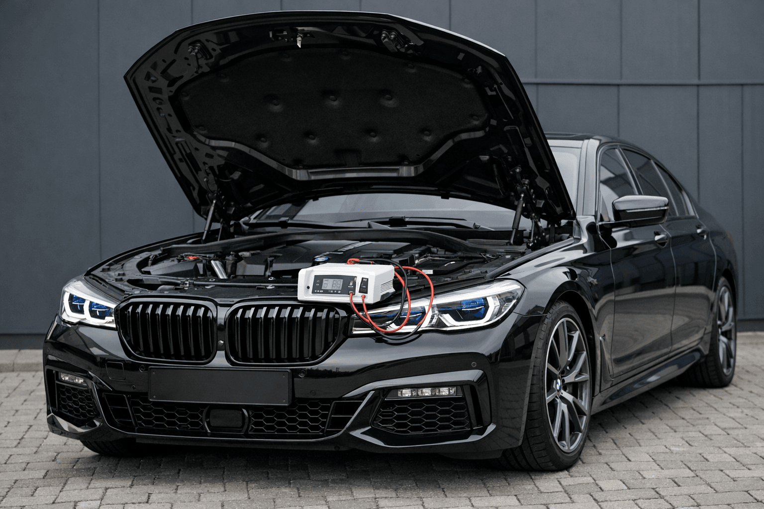 BMW Seria 7 G12 745Le M Sport PHEV z uniesioną maską — stabilizator zasilania GYS Flash 12112 na zderzaku przed pełnym autoscanem, sygnatura reflektorów Laserlight z niebieskimi akcentami