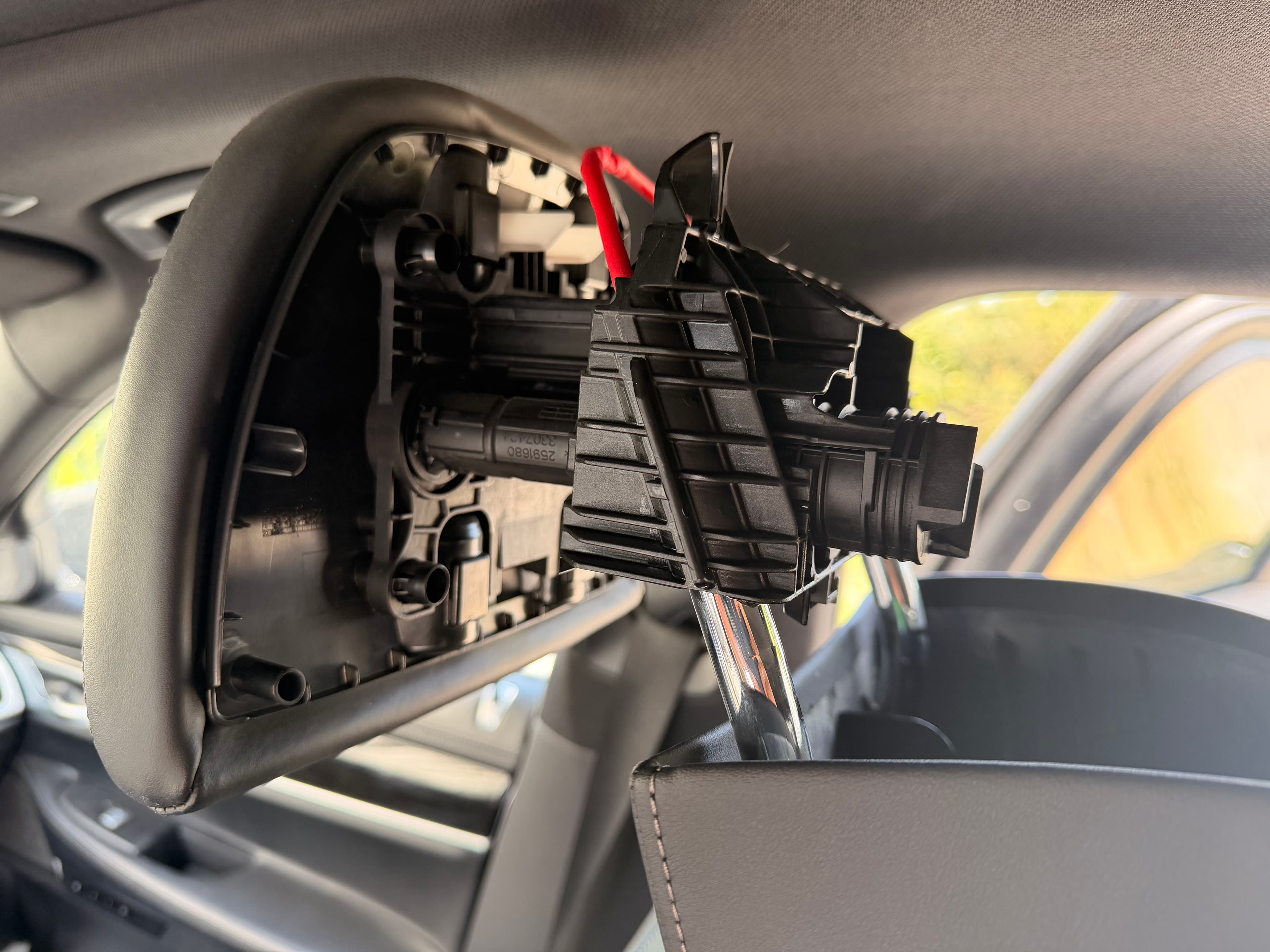 Aktywny zagłówek BMW G12 z otwartą obudową — widoczny mechanizm pirotechniczny: aktuator wysuwający zagłówek przy uderzeniu w tył oraz czerwony przewód wyzwalający nabój